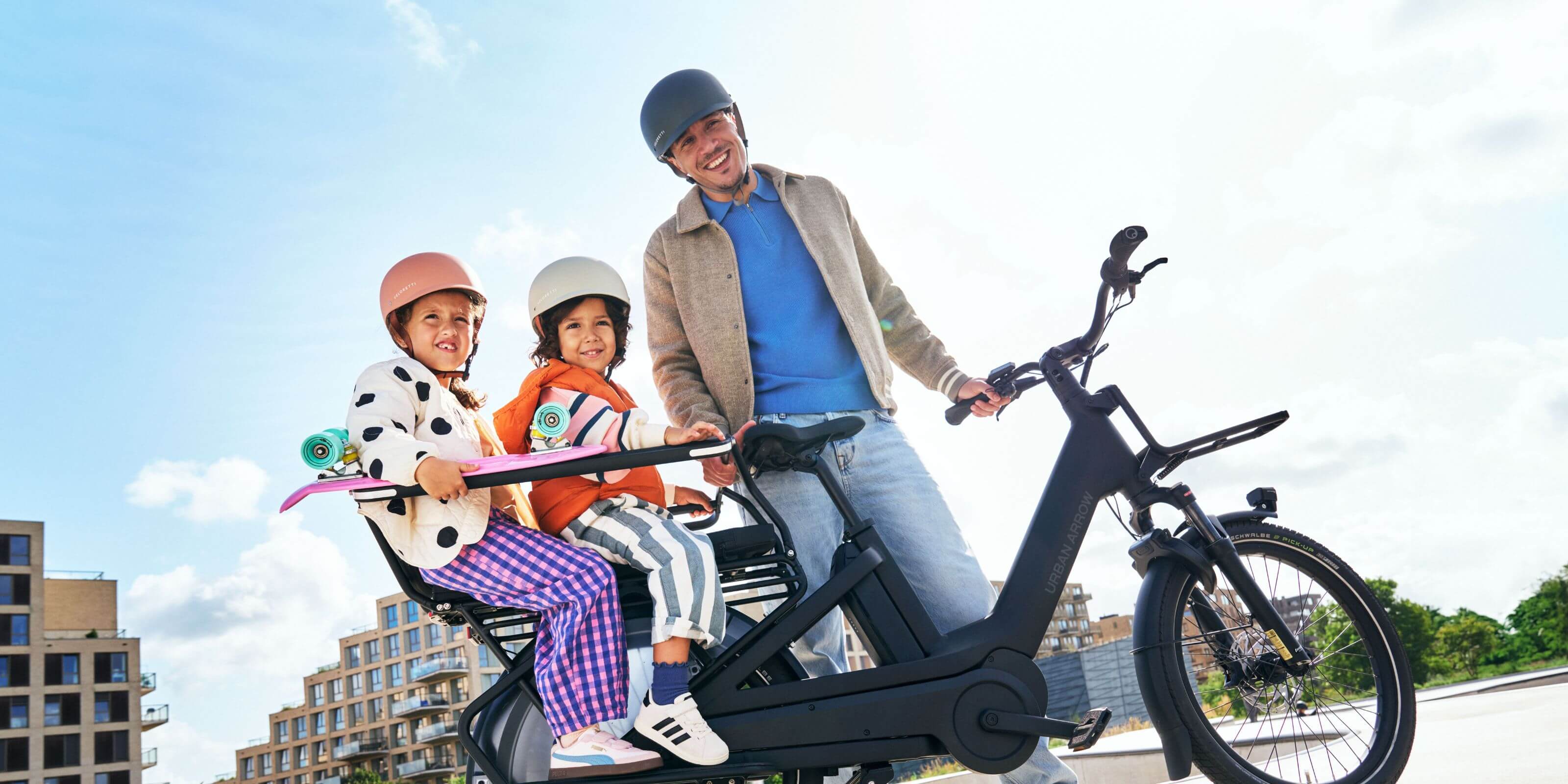 Side view of a father with the Urban Arrow Breeze electric cargo bike with two children seated on the rear cargo rack